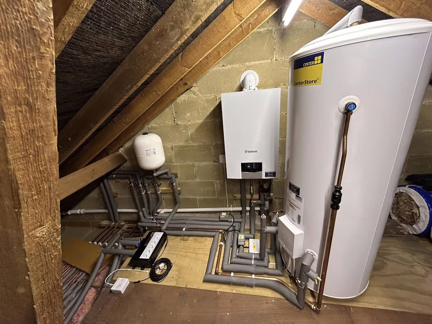 Boiler and unvented cylinder installed in a loft between the rafters with pipework run along the floor