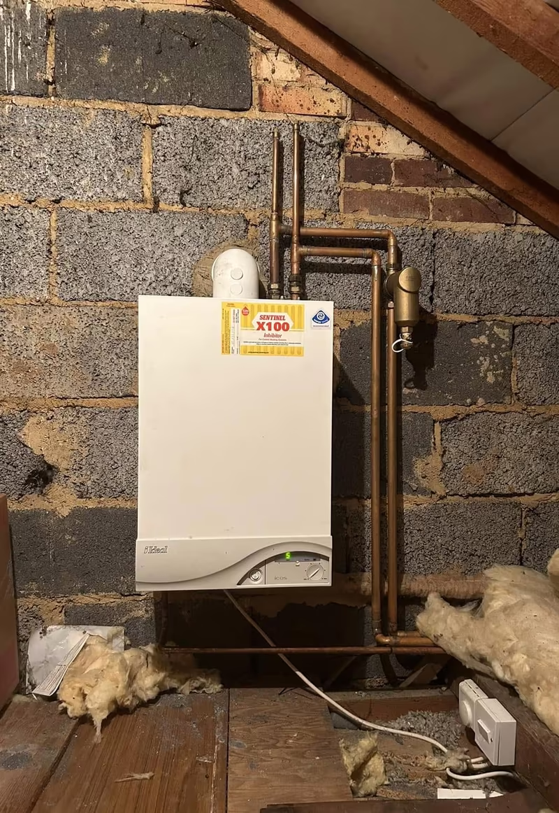 Boiler installed under the eaves in a loft with pipework and a system inhibitor label