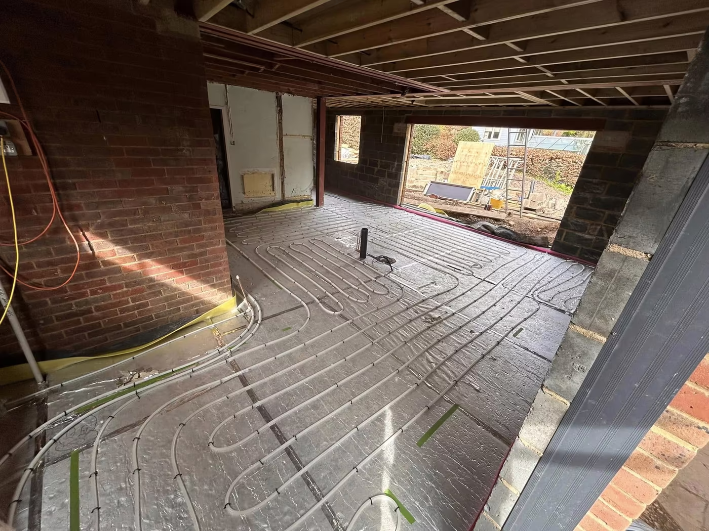 Underfloor heating pipework laid across the floor of a large extension with joists overhead